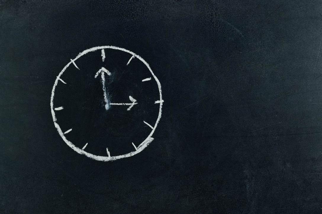 Photo d'un tableau sombre sur lequel des heures sont dessinées à la craie